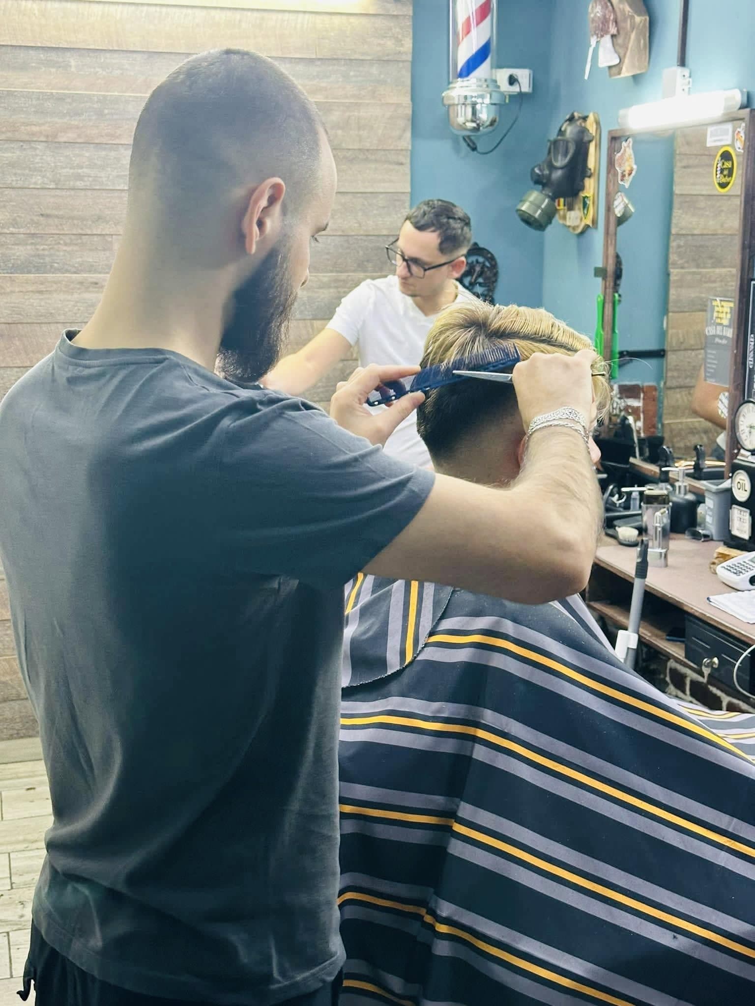 Frizer tunde un client în interiorul frizeriei, ambient cu oglindă și accesorii clasice