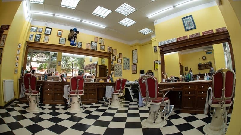 Interior cu scaune retro, oglinzi mari, pereți galben-verzui și produse de bărbierit pe rafturi