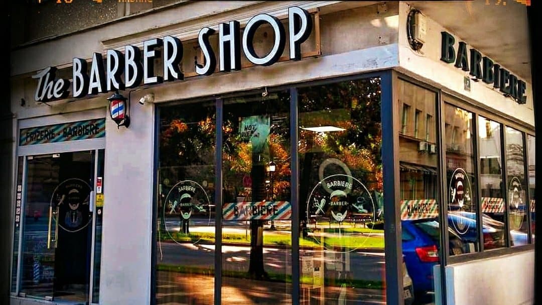Vedere exterioară a frizeriei, geamuri mari, inscripții și semn luminos